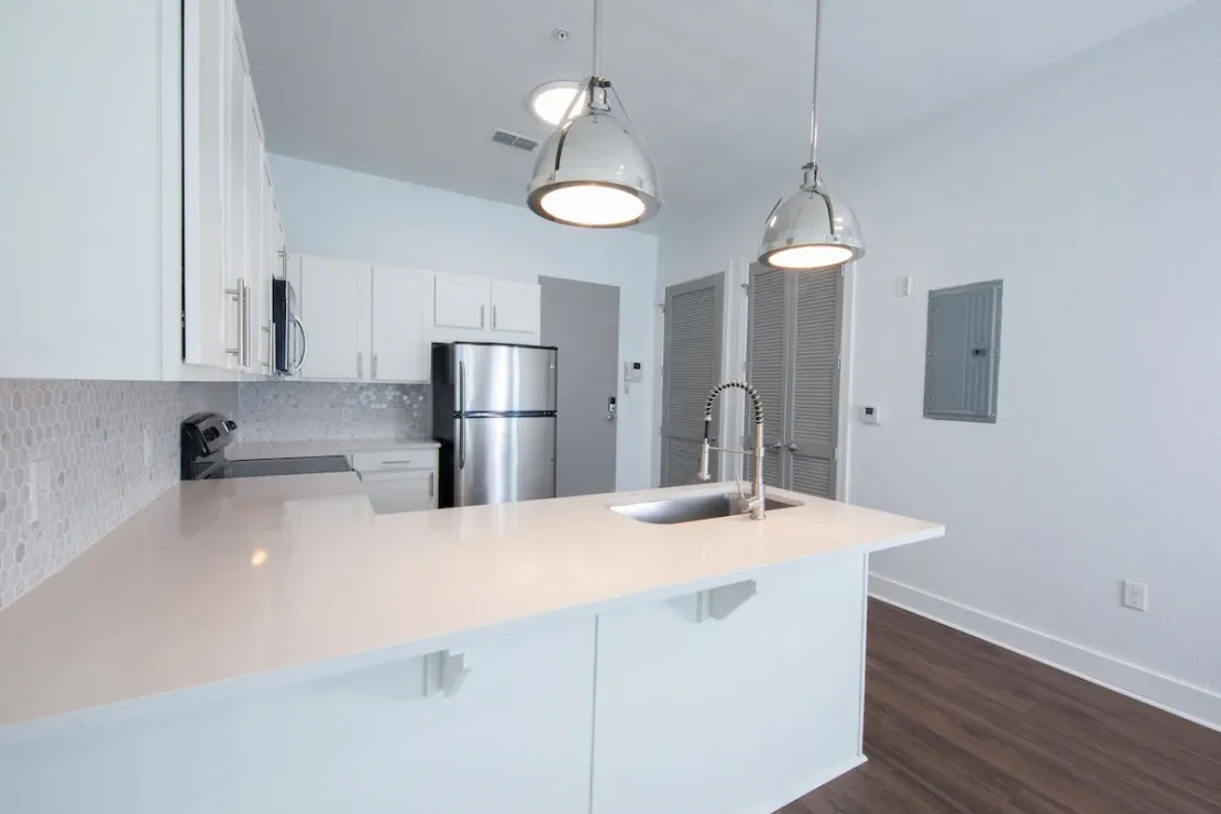 Apartment kitchen at Rise with light flat-panel cabinetry, geometric backsplash, and matte-black faucet